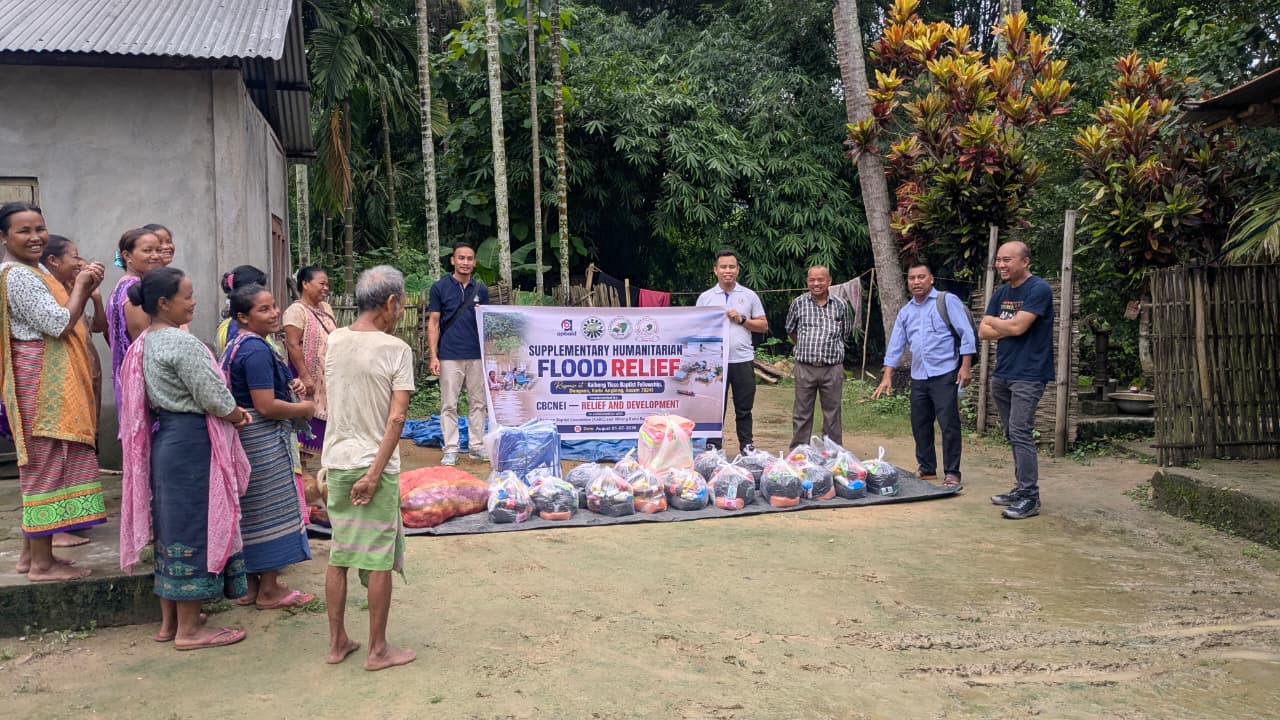 Community members gathered with flood-relief supplies and the distribution banner at Kaibong Tisso Village.